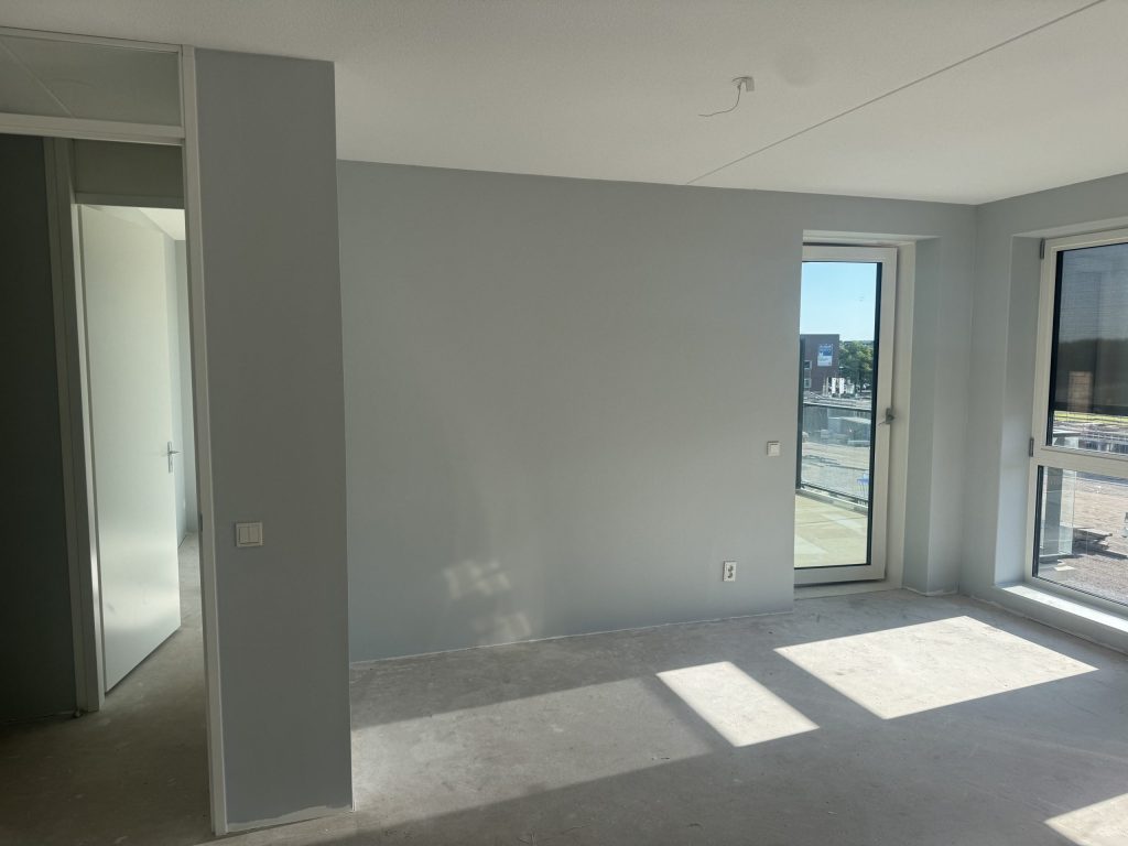 Nieuw appartement op een verdieping met lichtgrijze wanden, een balkondeur en zon op de betonvloer
