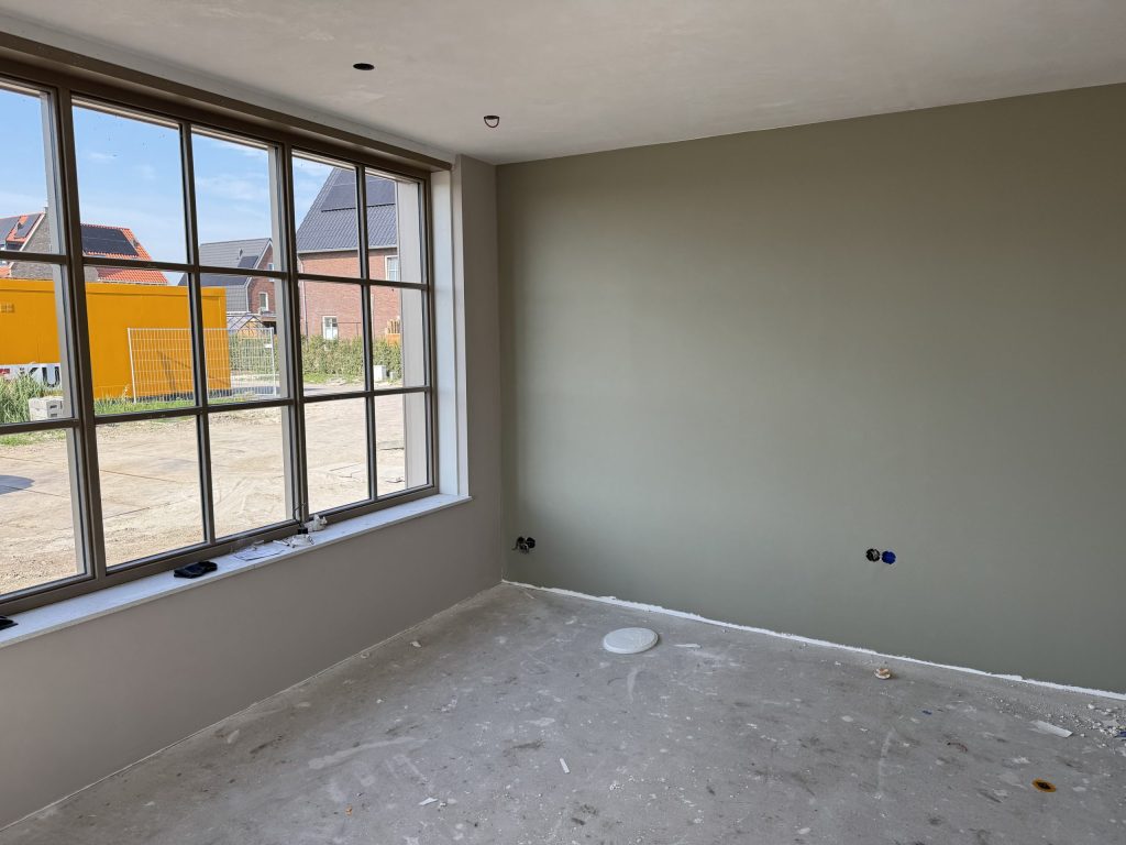 Egaal gesausde grijsgroene wand naast een breed raam in een nieuwe kamer