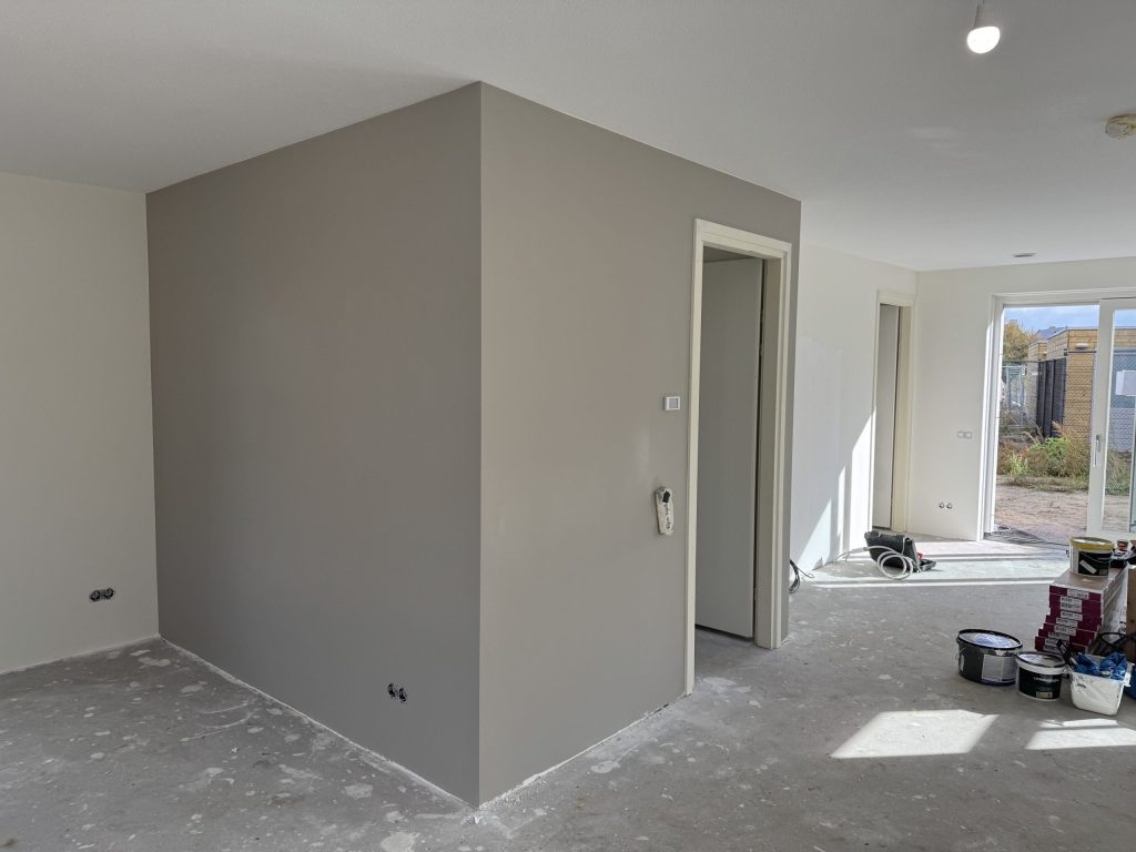 Pas gesausde grijze wand in een open benedenverdieping met verfemmers en vloerdozen bij de tuindeur